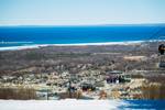 view of the chairlift at blue mountain in winter time with the vibrant blue of georgian bay in the distance